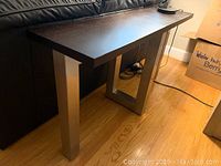 Side view of console table showing dark wood top and a stainless steel rectangular leg design.