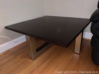 Front side view of coffee table showing dark wood top and stainless steel legs, positioned beside a black sofa on wood flooring.