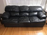 Front view of black leather couch showing three seats and padded arms