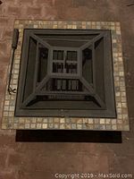 Top view showing the tiled table surface with fire pit insert and mesh screen cover with handle.