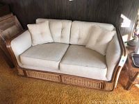 Front view of loveseat showing beige upholstery, tufted back cushions, matching pillows, wood and wicker frame.