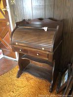 Child's wood roll top desk closed, showing front with two small drawers, round brass knobs, and bottom shelf.
