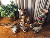 Overview photo showing artificial plant in brass pot, ceramic tiger cub, ceramic vase, resin roosters, and bark and pinecone birds, all placed on an orange carpet.