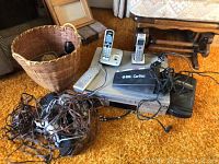 Photo showing Panasonic VHS/DVD player with remote, Black & Decker car vacuum, cordless phones, and wiring piled on a carpet.