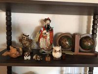 Various knickknacks displayed on shelf including a colorful Asian figurine, globe bookends with wooden frames, ceramic owls in brown and white, a small carved bird or shell figure, and ceramic bulldogs.