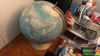 Photo of a vintage-style globe with muted blue and beige colors and various office supplies behind it on a desk.