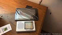 Top view of Kindle sealed in plastic wrap and Bell Howell portable radio on wooden surface