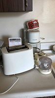 Photo showing the coffee maker, toaster, and chopper appliances together on countertop with visible power cords and instruction manual for toaster.