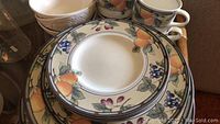 Close-up photo showing the Mikasa ceramic plates and mugs with peach and grape fruit pattern and dark blue rim.