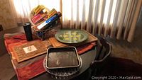 Multiple food trays arranged on a wooden table with patterned autumn-themed tablecloth, including round and rectangular trays and a woven basket holding packaged items.