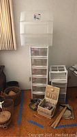 View of multiple plastic storage boxes including a tall 5-drawer unit, 3-drawer unit, stacked clear lids, sewing box with supplies and baskets on floor.