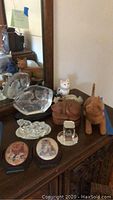 Overview of various cat decor items including carved wood figurines, ceramic cats, glass sculptures, and wooden storage box on a wooden table surface.