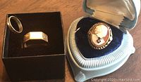 Photo showing all three rings together with the cameo ring in a blue cushioned box and two gold color rings on black display boxes.