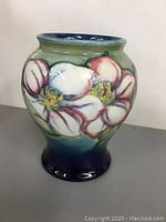 Front view of Moorcroft vase showing raised pink and white flower design, green background.