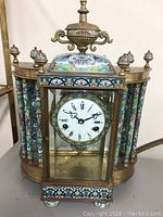 Full front and side view of brass and cloisonné mantel clock showing pillars, dome, feet and porcelain dial