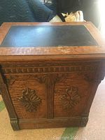 Closed oak cabinet with ornamental carved front panels and black inset top