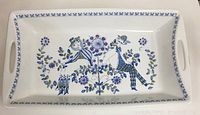 Top-down view of the rectangular white ceramic dish showing the full design of two stylized human figures in blue, green, and purple floral surroundings.
