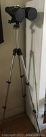 Full view of black Skymaster binoculars mounted on silver tripod against wall