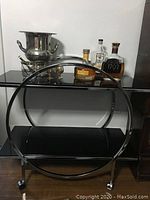 Full view of chrome bar cart showing circular frame, two shelves and caster wheels