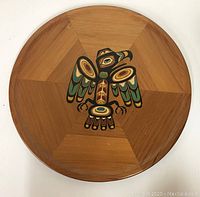 Photo of the round cedar plate with painted Indigenous eagle design in the center, showing full plate surface and wood grain.