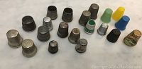 Lot of 20 thimbles arranged on a white surface, showing metal and plastic types in various colors and sizes.