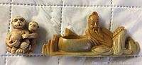 Both small Asian carvings shown side by side on a white quilted background.