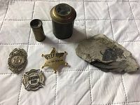Overall view of three badges, two lenses, and fossil stone on white quilted background.