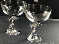 Two clear glass martini glasses with dolphin-shaped footed stems, shown from front angle.