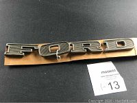 Front view of four metal emblem letters spelling 'FORD' on cardboard backing