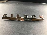 Full view of the Gilson Snow Bird vintage car emblem on a black surface