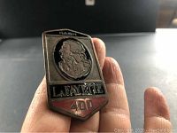 Close-up of front of Nash Lafayette 400 metal car emblem showing details of soldier profile, text, and enamel colors.