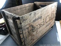 Photo showing side view of the heavy wooden crate with faded Pepsi Cola branding and surface wear.