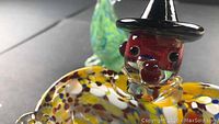 Close-up front view of clown candy bowl showing red face with black hat and mottled glass body in yellow, white, and brown colors.