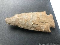 Clear close-up of the stone arrowhead highlighting the pointed tip, overall flaked texture, and notched base for hafting.