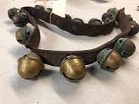 Close-up image showing brass sleigh bells attached to worn leather strap, highlighting wear and tear.