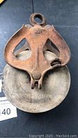 Front view of the antique pulley showing iron frame with rust and wooden pulley wheel
