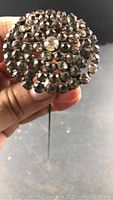 Front view of round vintage rhinestone cluster hat pin held in hand, showing prong-set rhinestones.