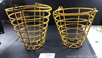 Two antique yellow wire egg baskets with handles side by side, viewed from front.