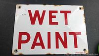 Full front view of the porcelain enamel wet paint sign showing the red letters on white background and rust spots near edges.