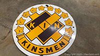 Full view of the circular Kinsmen porcelain sign showing central logo, maple leaf border and mounting hole.