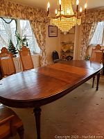 Photo of rectangular wooden dining table in dining room with four ornate high-backed chairs and chandelier overhead.