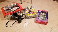 Photo showing Konica camera with strap, Canon printing calculator in original box, portable gas stove box labeled Chef, and plastic box containing assorted fabric paints.