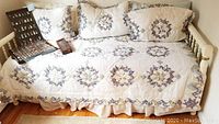 Twin size white wooden trundle bed with floral quilt, pillows and linen on the main mattress. Wooden frame is visible with turned legs.