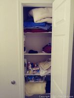 Closet shelves containing folded linens and some toiletry bottles