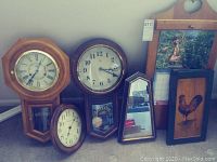 Three wall clocks including two Regulator style clocks and one round wooden wall clock, small mirror, wooden calendar frame, and rooster wall art displayed.