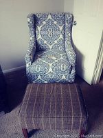 Wingback chair upholstered in blue and white patterned fabric with a plaid ottoman in front