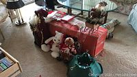 Wide shot of box containing artificial Christmas tree with two stands, seasonal stuffed animals including polar bear and reindeer, Santa figurine on sleigh, Christmas cards, and tags underneath glass table.