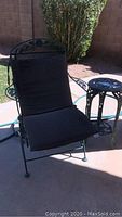Metal outdoor chair with black frame and brown cushions, set on patio surface with shadow cast.