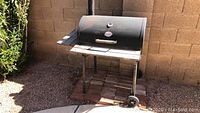 Photo of the CharGriller grill and smoker showing the full unit with lid, side shelves, and wheels on the ground in outdoor setting.