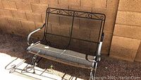 Front angle view of black wrought iron bench showing mesh seat and decorative scrollwork on backrest and armrests.